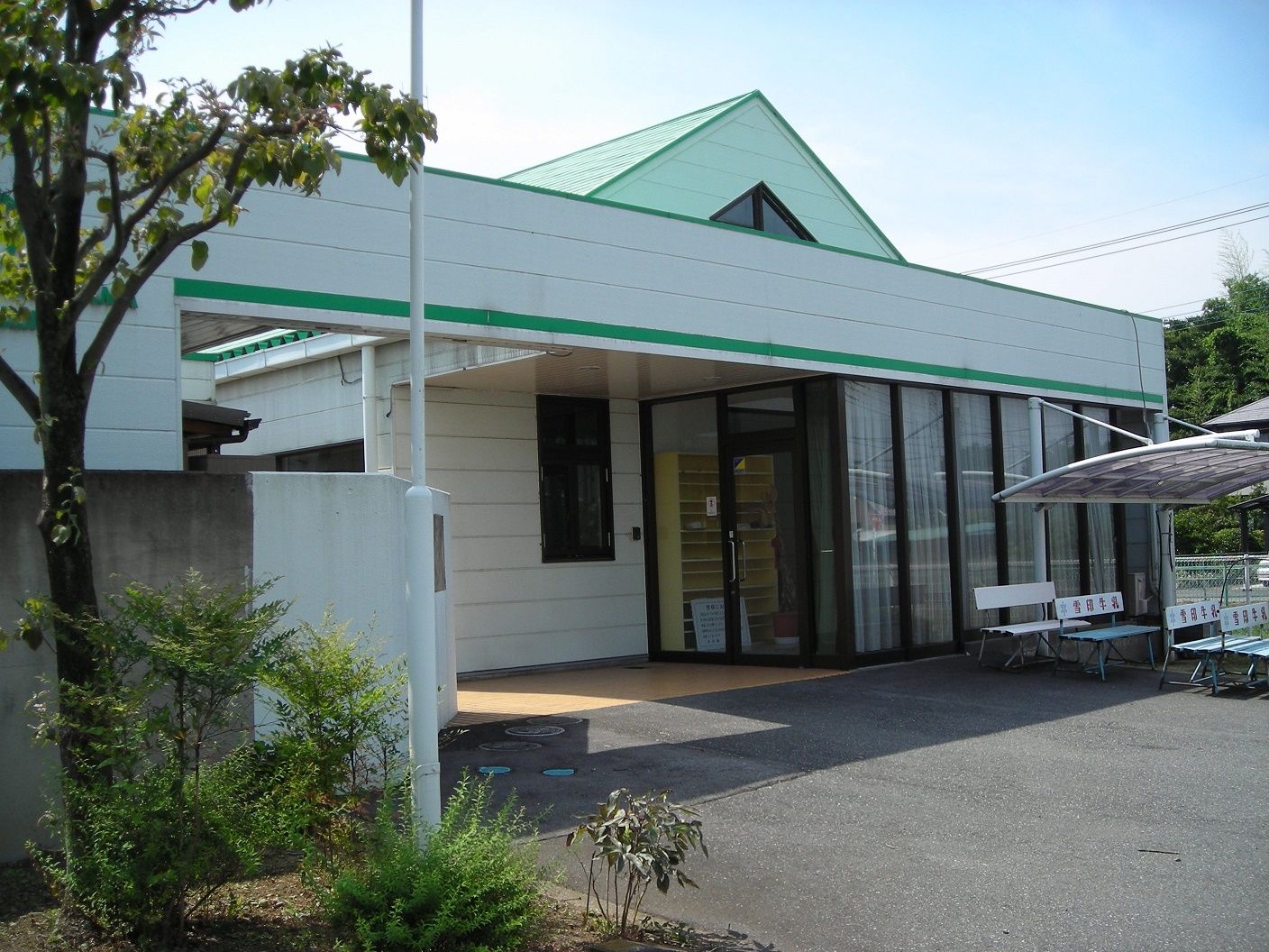 ライトグリーンの屋根が付いた平屋建ての建物の外壁は白く、建物の前にはベンチなどが並んでいる。