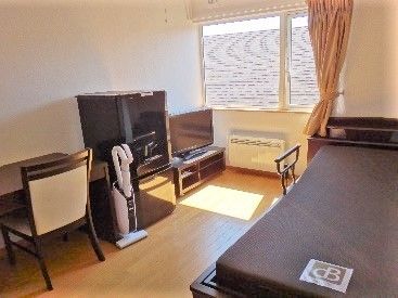 右側にはベッド、左側にはテレビ冷蔵庫・掃除機・デスクセットなどが置かれている。