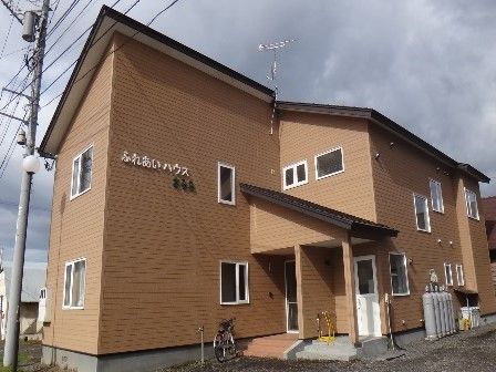 茶色の建物は２階建てで、外壁にはハウスの名前が書かれている。