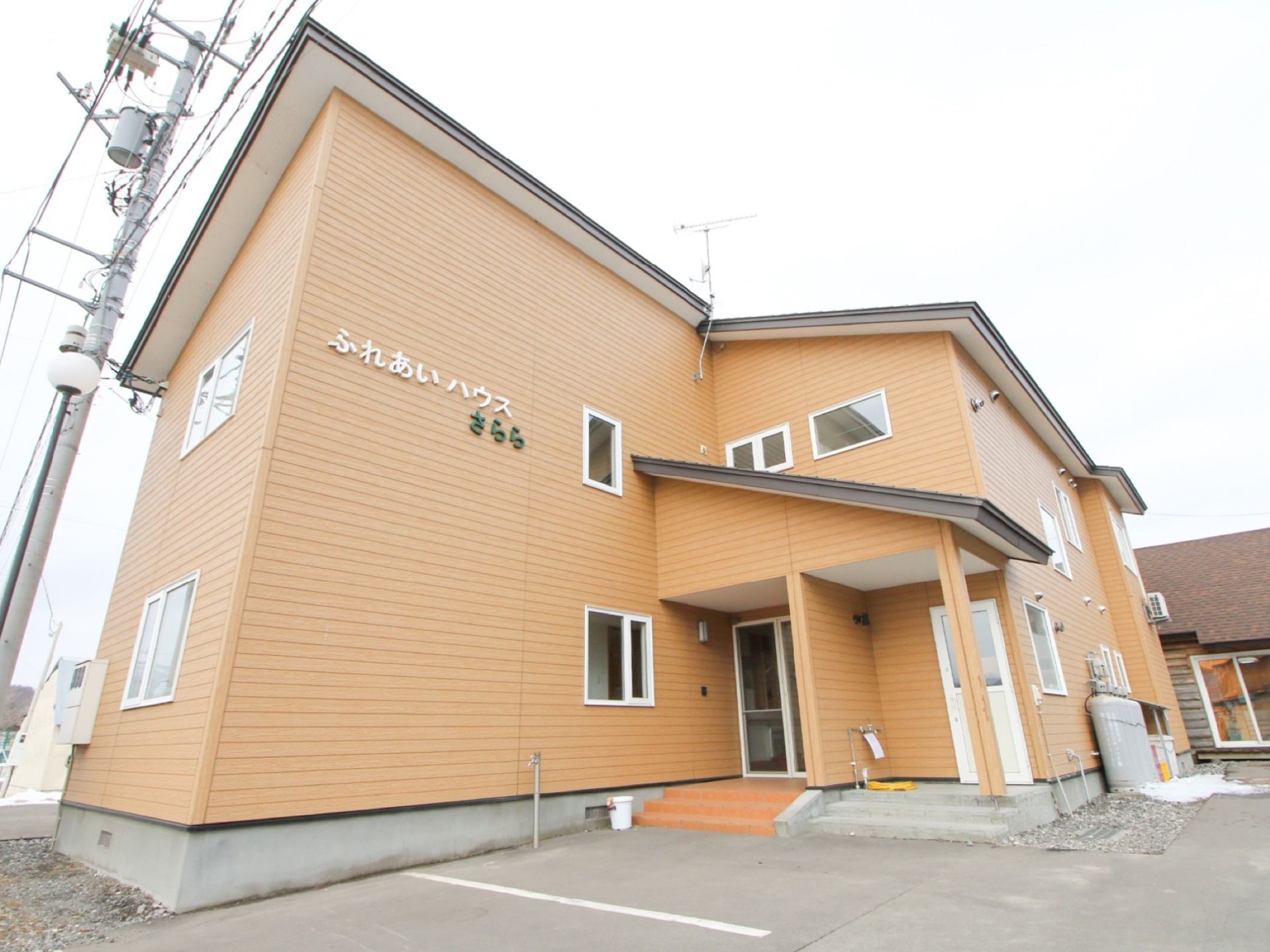 アットホームな雰囲気のある２階建てのオレンジ系の建物である。周辺には駐車場があり、アスファルトで舗装されている。
