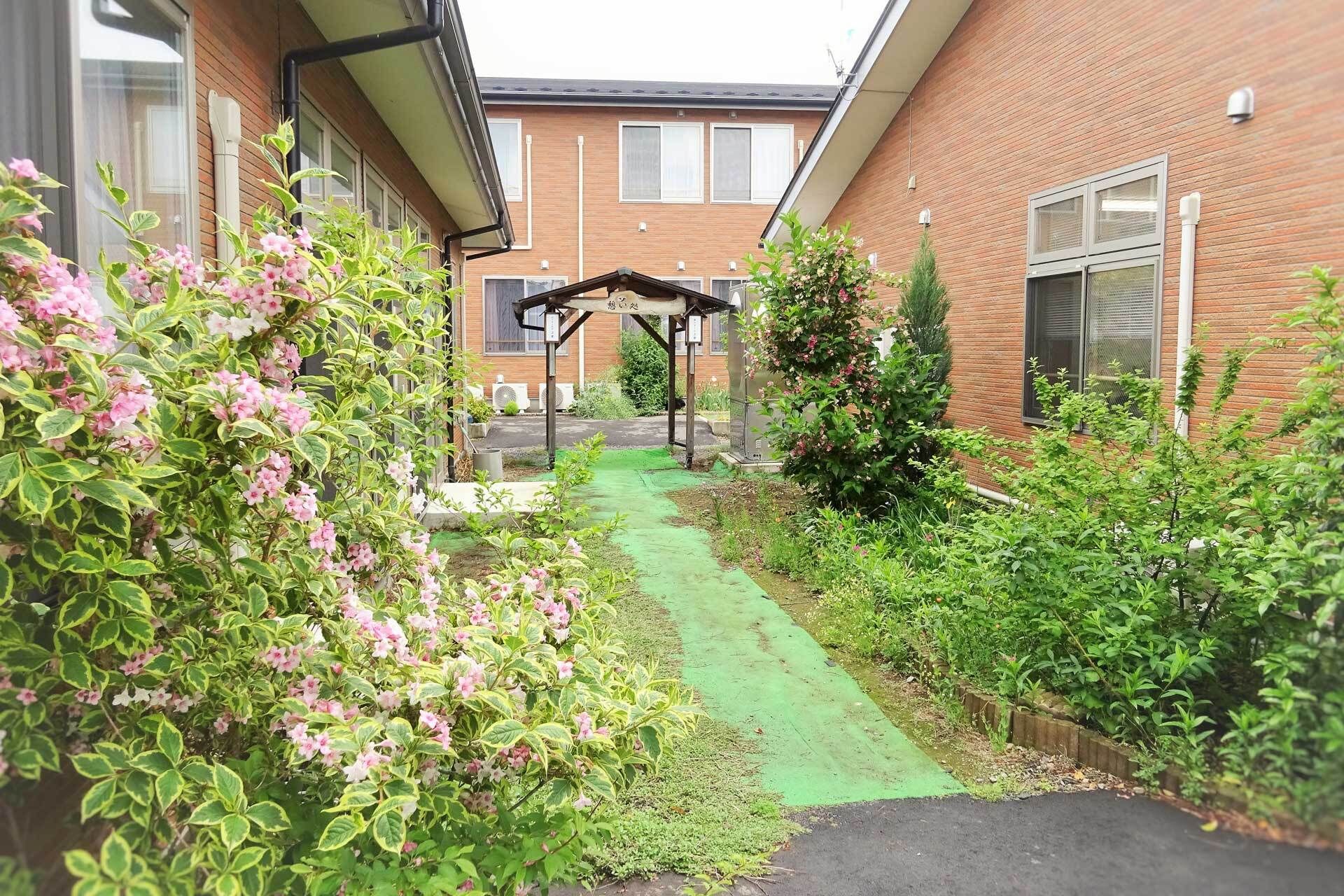 ブラウンの建物の周りにはたくさんの草木が植えられていて、中央には東屋のようなものもある。