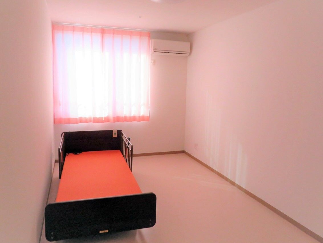 ピンクのカーテンが付いた窓がある個室の部屋には介護ベッドやエアコンがあり、全体的にピンクでまとめられている。