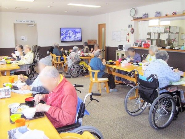 施設内の食堂で食事をとっている高齢者の様子。車いすに乗っている人もいるのがわかる写真