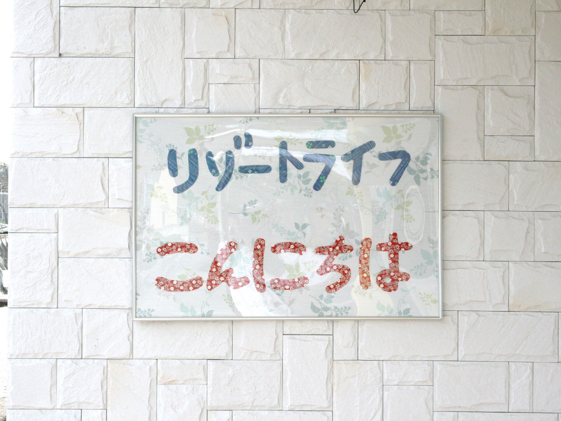 「リゾートライフ　こんにちは」と青と赤の文字で書かれた紙が貼られている外壁。