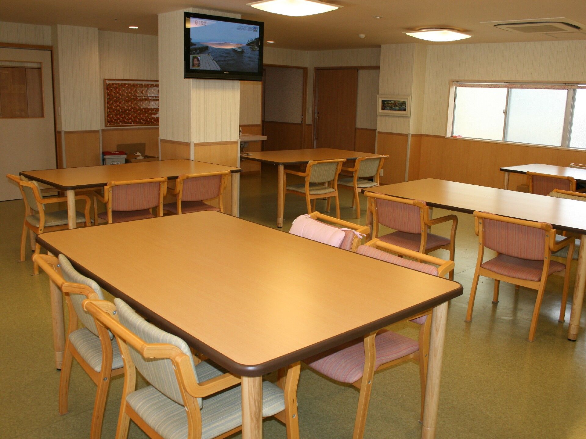 木製のダイニングテーブルが複数置かれた食堂には大きな壁掛けテレビが設置されている。