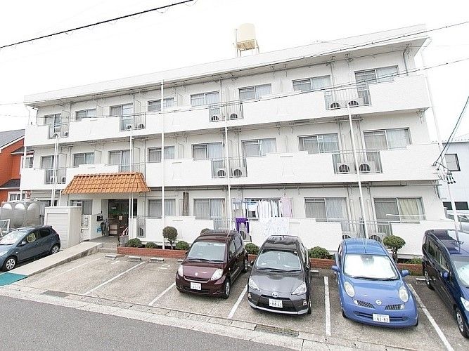 3階建ての建物にはベランダや駐車場が付き、玄関の周りにある花壇には木や花も植えられている。