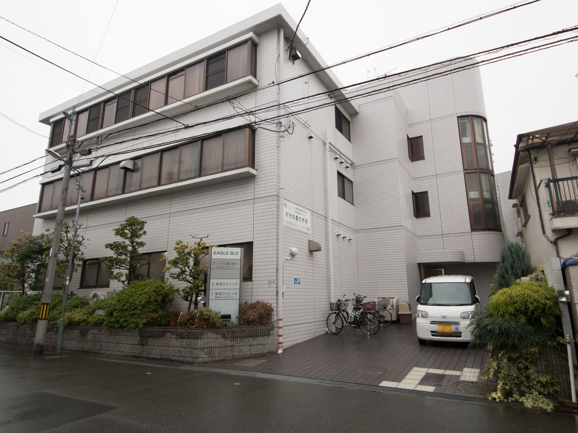 オフホワイトのタイルがはめられた外壁は、清潔な印象である。建物は３階建てで、手前には樹木が植栽されている。
