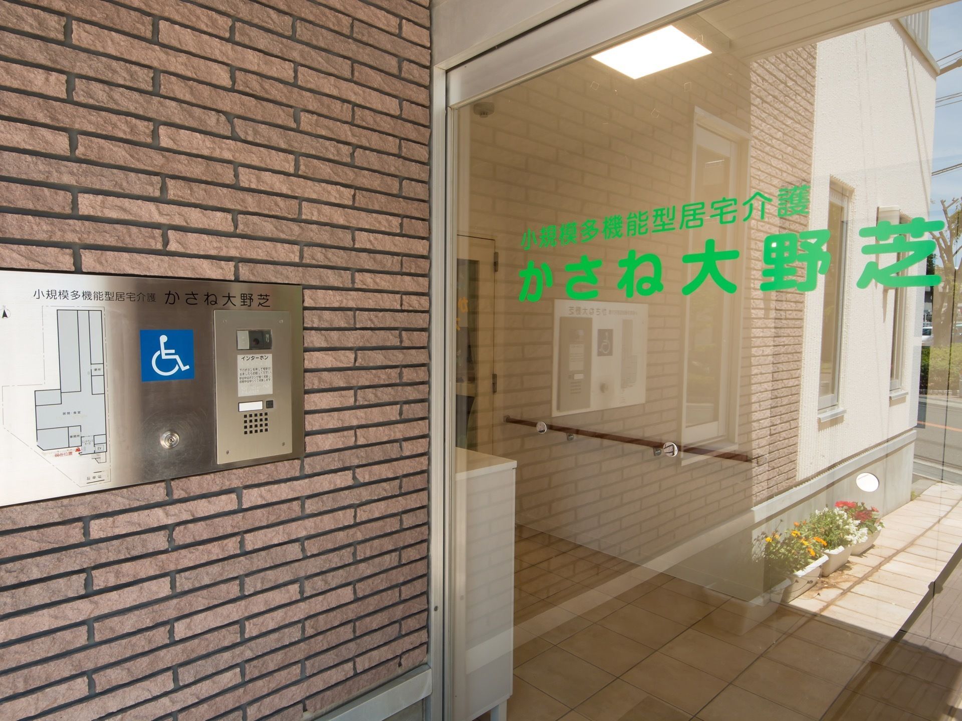 正面玄関自動ドアの様子。ガラス張りなので館内の様子が見えており、表面には施設名が緑の文字で印刷されている。