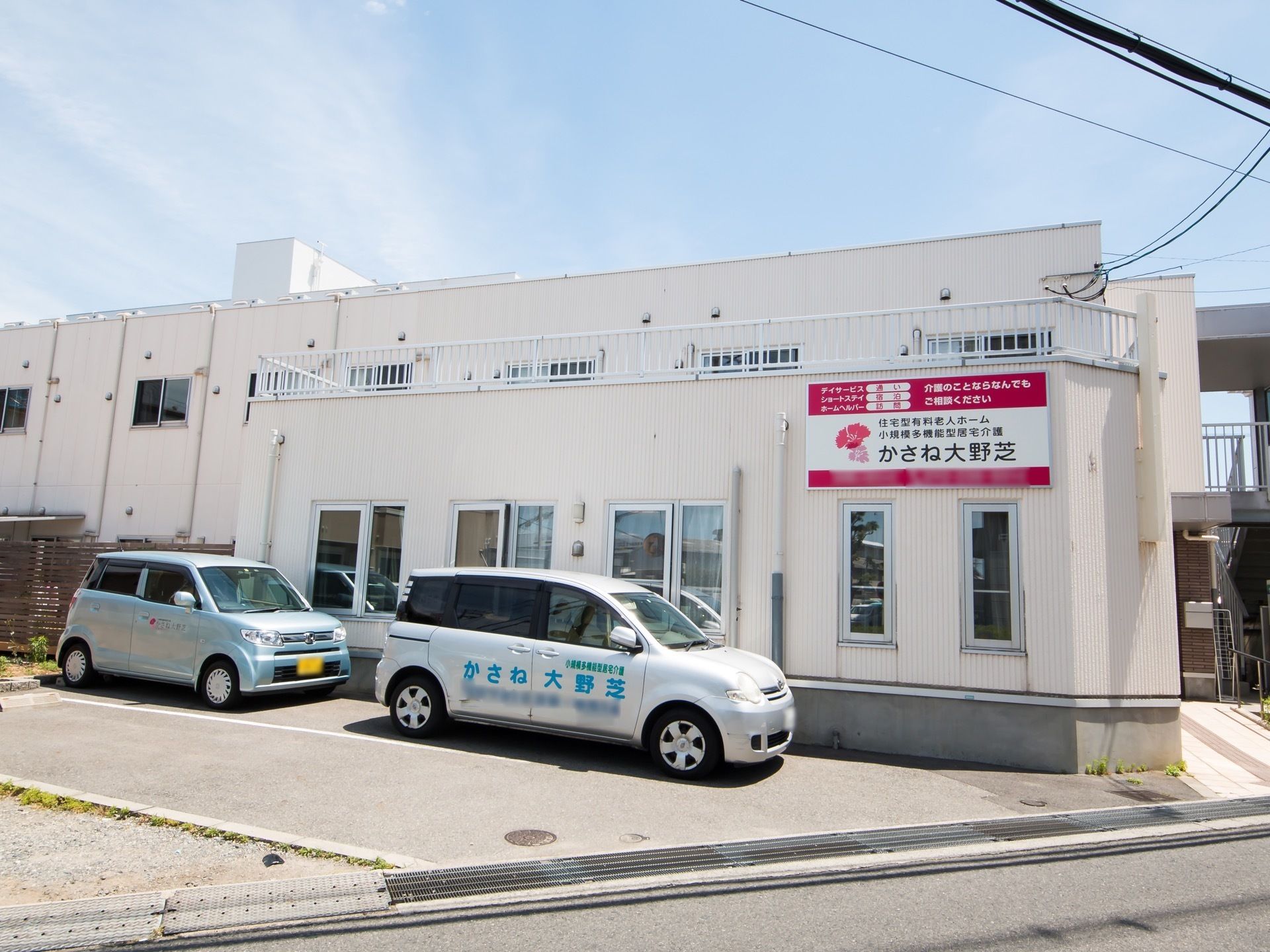 区画の関係上、建物は接する公道に対して斜めのレイアウトになっている。駐車場には施設所有の送迎車が停めてある。
