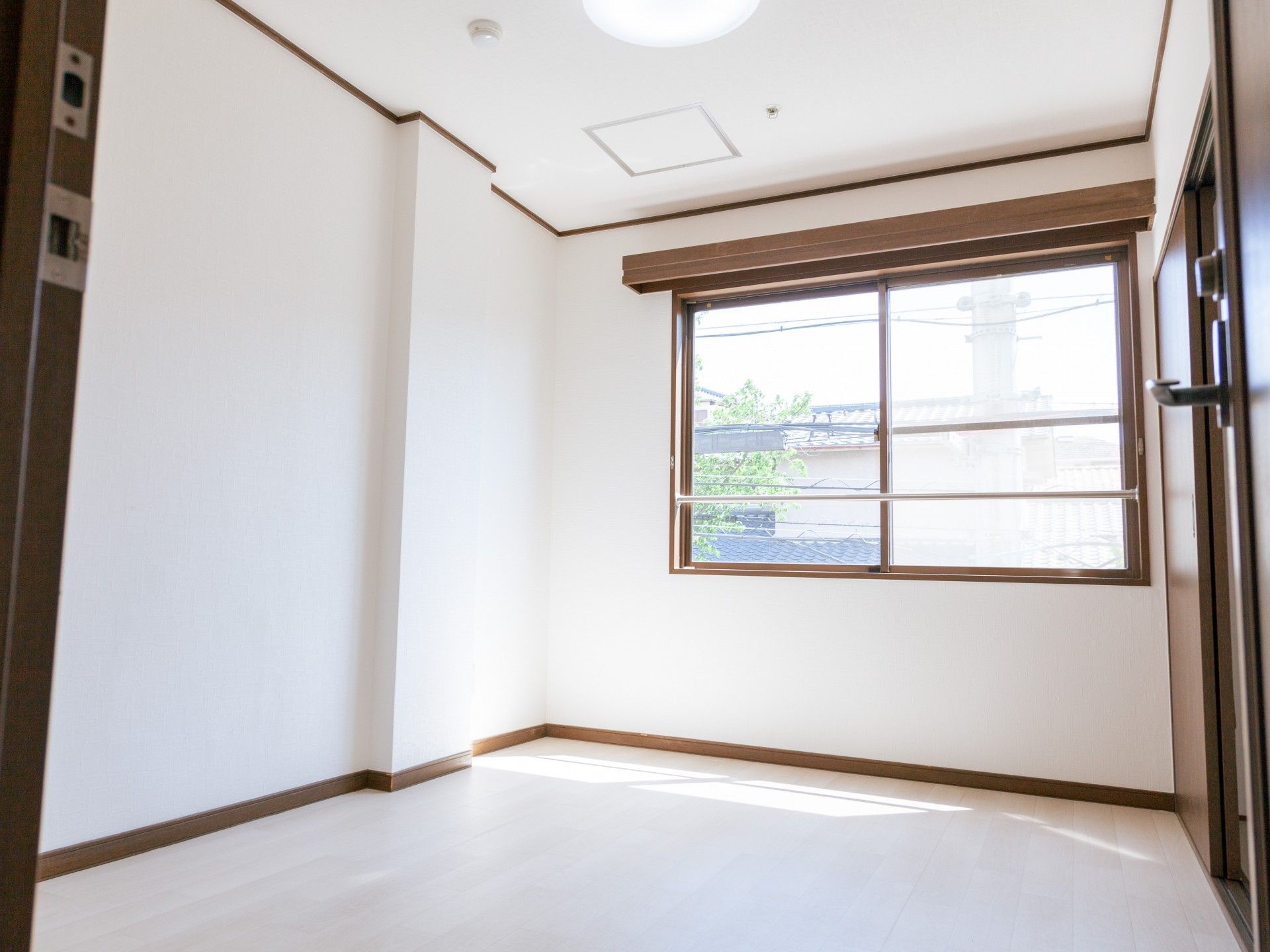 レースカーテンとカーテンが付いた窓があるフローリングの部屋には寝具付きのベッドやテレビがある。