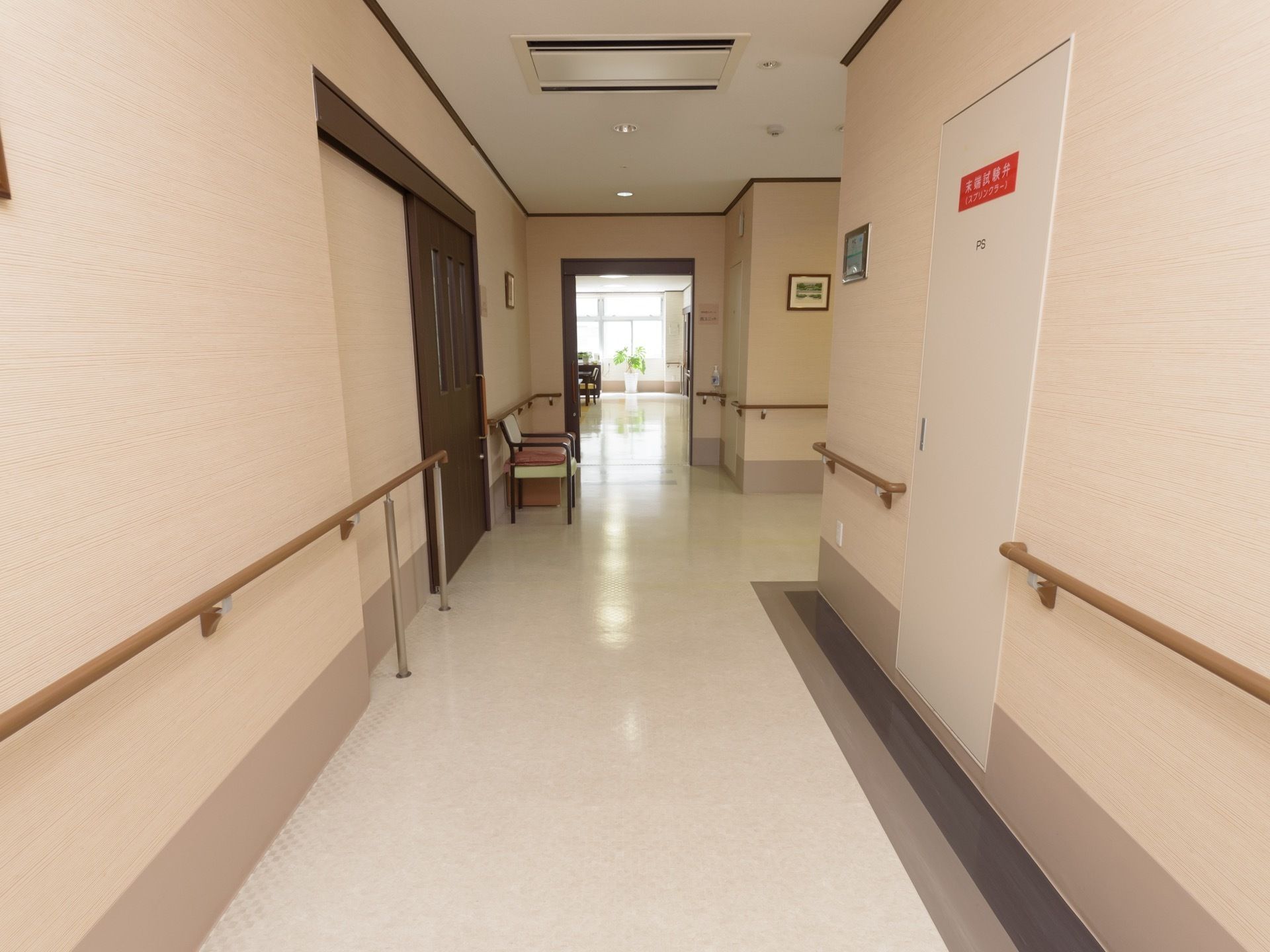 左右両側の壁に手すりが設けられた廊下で、途中に椅子が1脚置かれている。壁に小さめの絵画が飾られている。