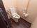 温水洗浄便座が1台設置された個室トイレで、壁に操作パネルがある。その左側にナースコールが用意されている。
