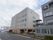 5階建ての白とオレンジの外壁の建物で、大きな道路に面して建てられている。ひさしの下に数台の車が停車している。