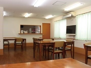 濃い色合いのフローリング仕様のリビング。テーブルと椅子が並んでいる施設内