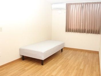 ベッドがひとつだけ置いてある小さな部屋の様子。カーテンがかけられた窓、エアコン