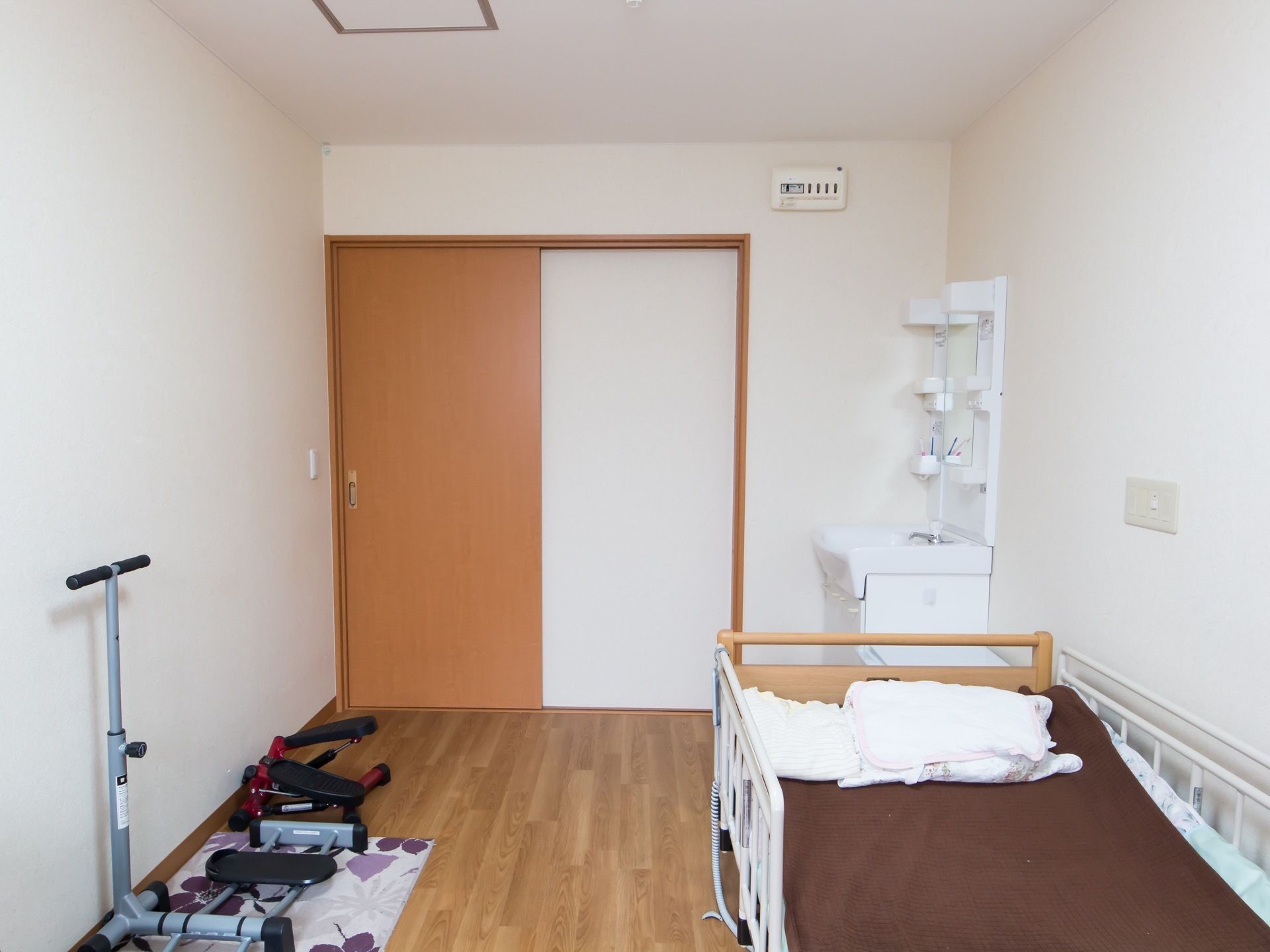 左の壁側に足の運動が行える健康器具が2台並べて置かれている。右の壁側に電動ベッドが1台設置されている。
