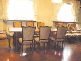大きな窓があり明るい食堂には背もたれの高い椅子が6脚置かれたダイニングテーブルと花柄の椅子が置かれている。