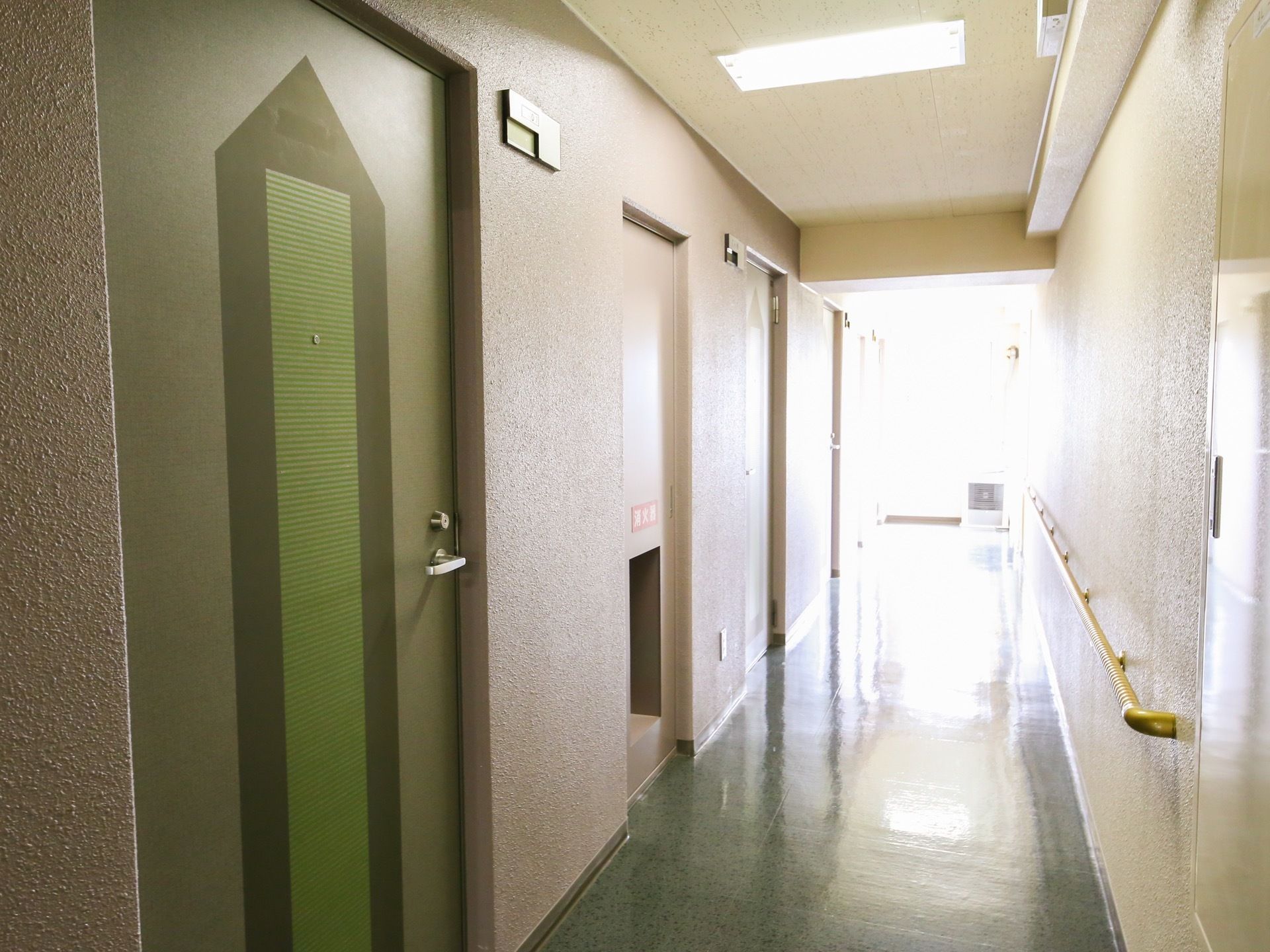 通路の左側の壁面には、緑色のドアが並んでおり、消火栓が設置されている。緑色のドアには鍵穴とドアノブがある。