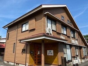 三角屋根が付いた２階建ての建物はブラウン系の外観で日当たりのいい場所に建っている。