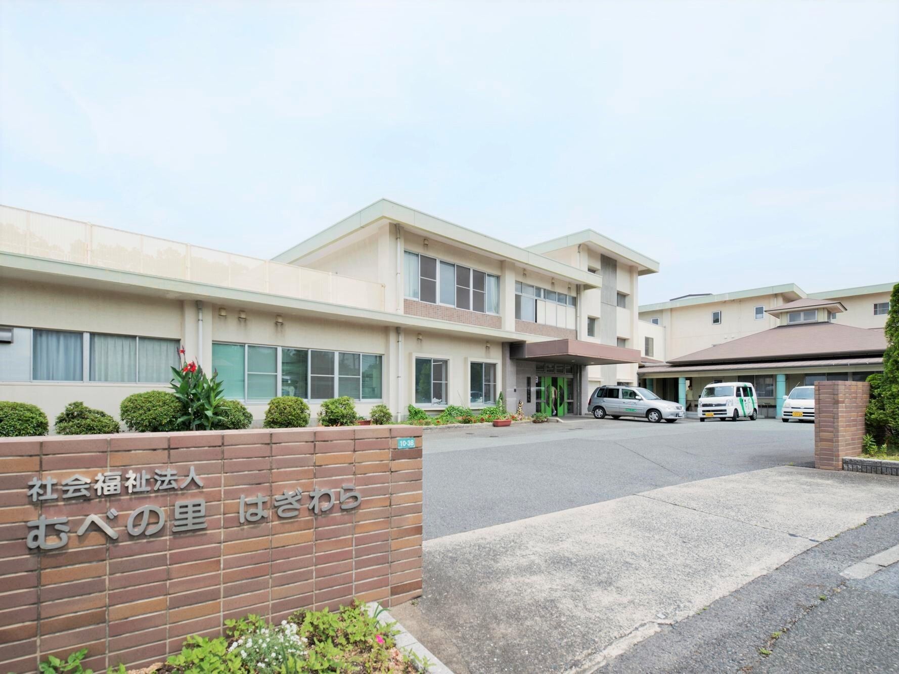 駐車場付きの建物は一部平屋建ての2階建て。門はレンガでできていて、ホーム名が書かれている。