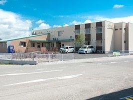ベージュを基調とした２階建ての建物は横に長く、駐車場もある。