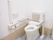 便座に背もたれと手すりが付いたトイレは広く、壁にも手すりが付いている。便座のふたはない。