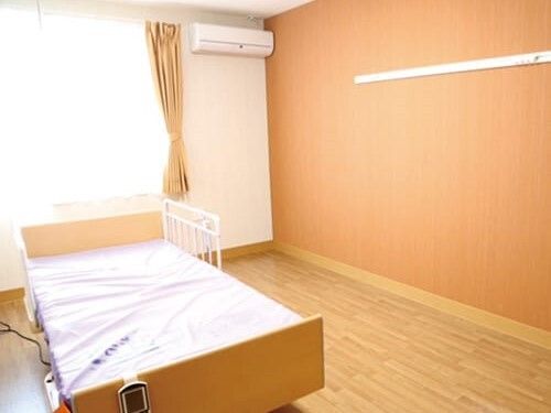 ピクチャーレールやエアコンが付いたフローリングの部屋には寝具付きのベッドがある。