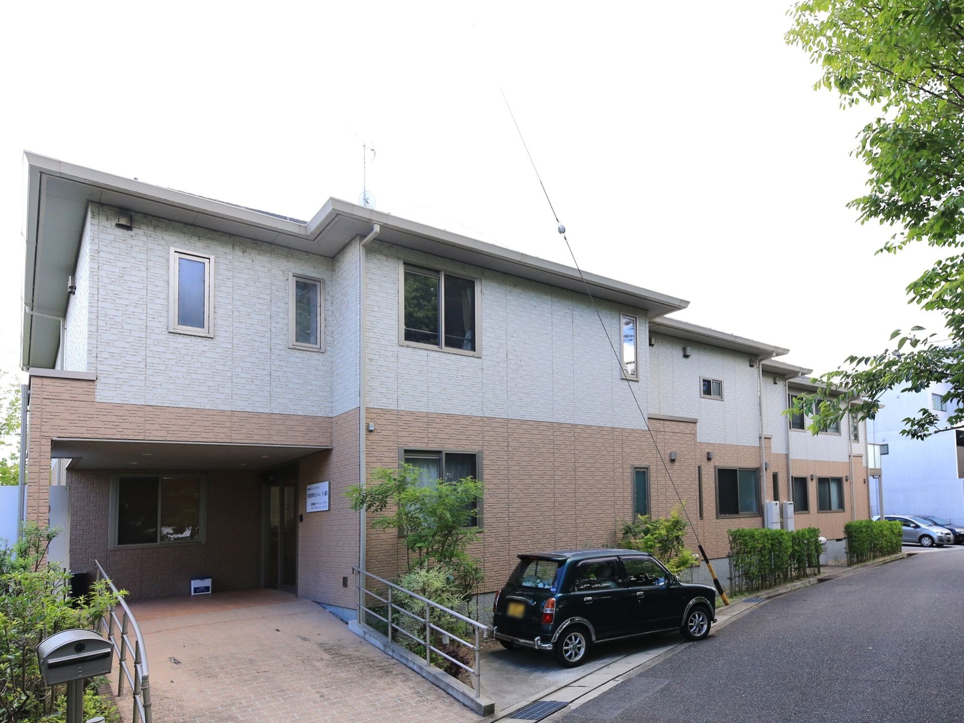淡いカラーで施された2階建ての施設である。駐車スペースには1台車が停められている。外壁には施設名が記された看板が設置されている。