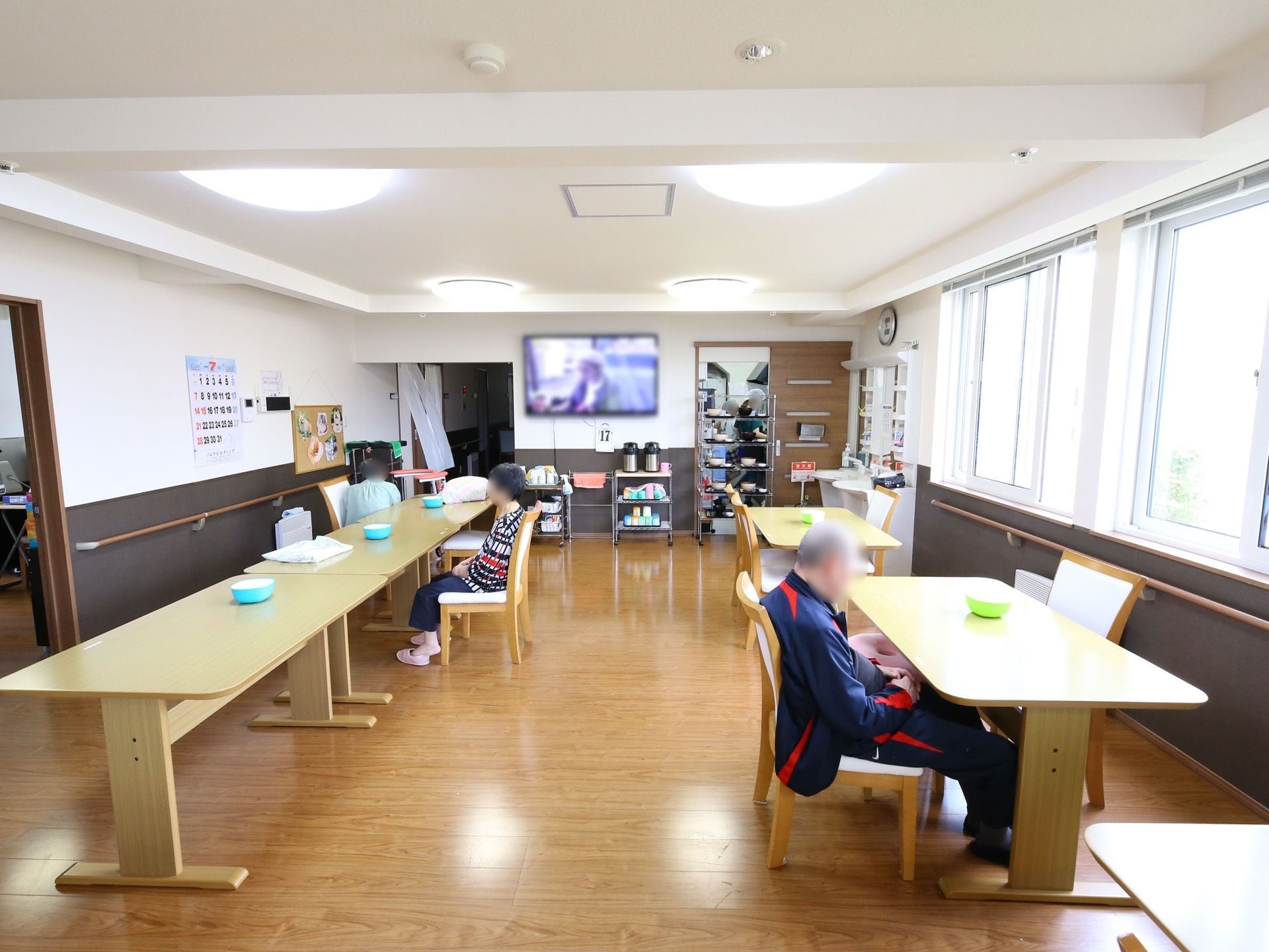 テレビが設置されている開放的な食堂である。ダイニングテーブルが複数セッティングされており、入居者様が思い思いの時間を過ごしている。