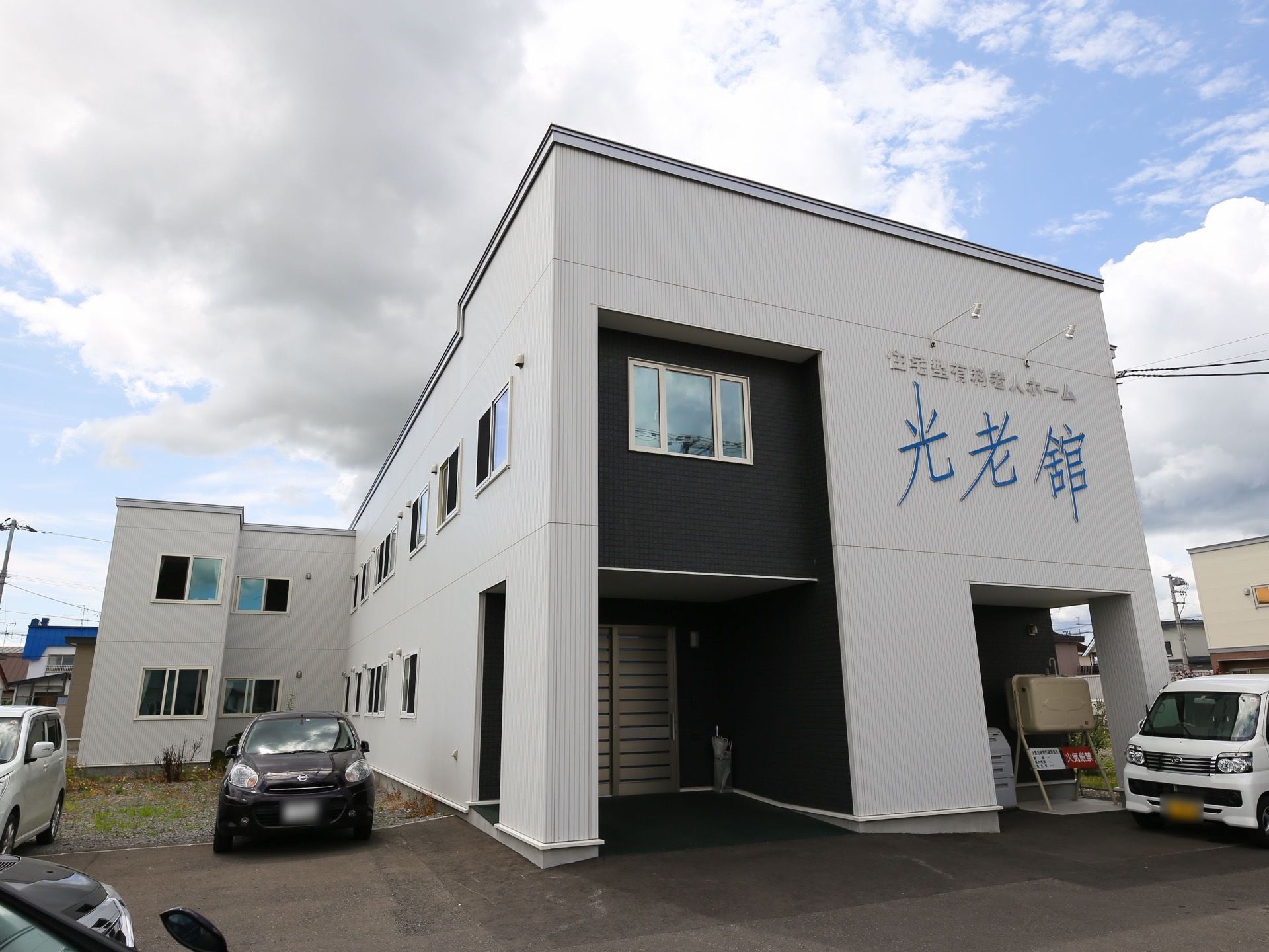 黒と白を基調としたスタイリッシュな外観の施設である。アスファルトで舗装された駐車場には、複数台の車が停められている。