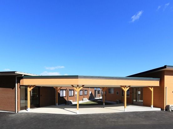 青い空の下にブラウンの平屋建ての建物があり、玄関前には車寄せもある。