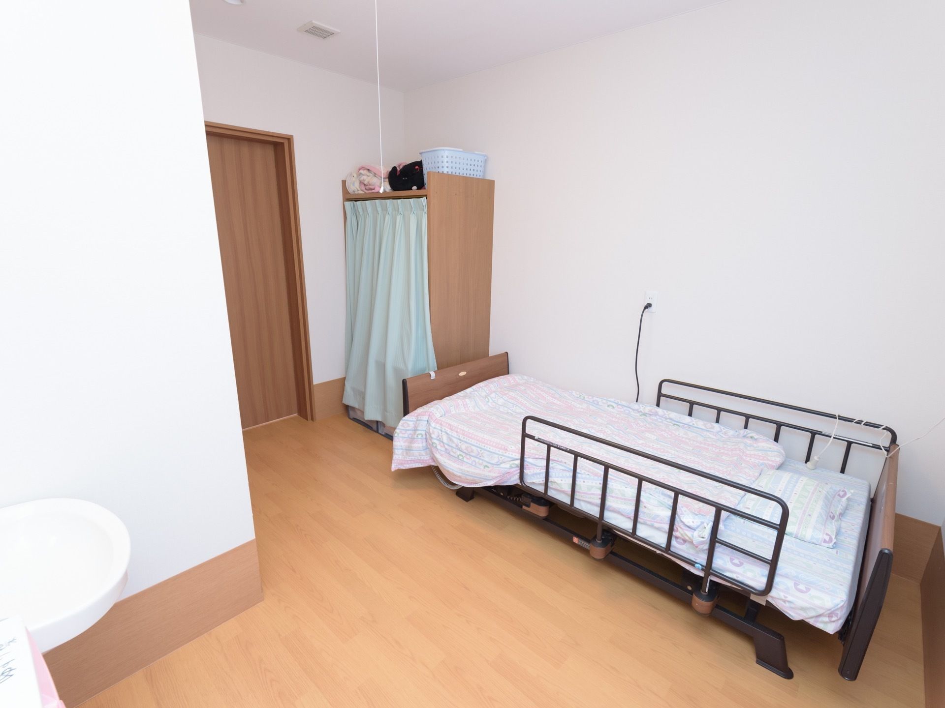 部屋の入口付近に収納棚が置かれ、前面はカーテンでカバーされている。両側に柵の付いたベッドがある。壁際に洗面台がある。