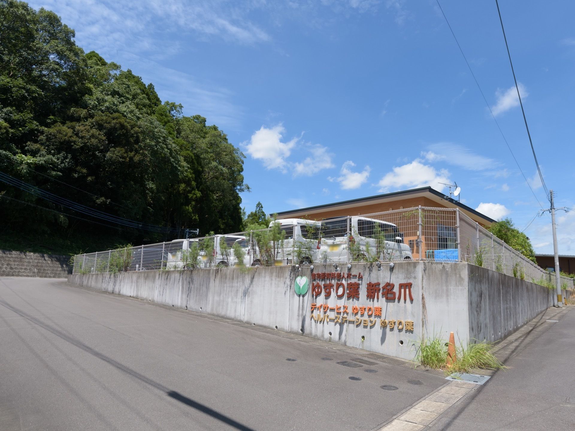 施設は公道より一段高い位置にある。敷地脇のコンクリート壁に大きく施設名が書かれている。建物の手前に駐車場が設けられている。