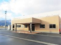 多き雨除け用の梁が印象的な建物。やわらかい色合い、低めの高さ、駐車場スペースた写っている