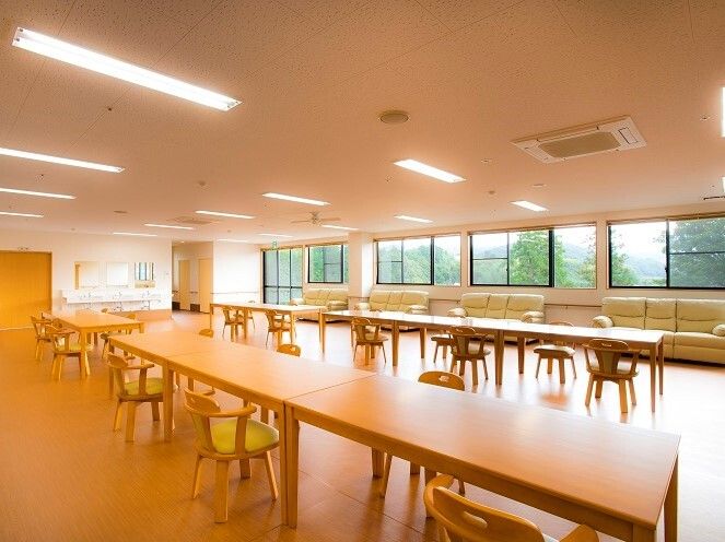 木製のダイニングテーブルが複数置かれたリビングダイニング。窓際にはソファがずらりと設置されている。