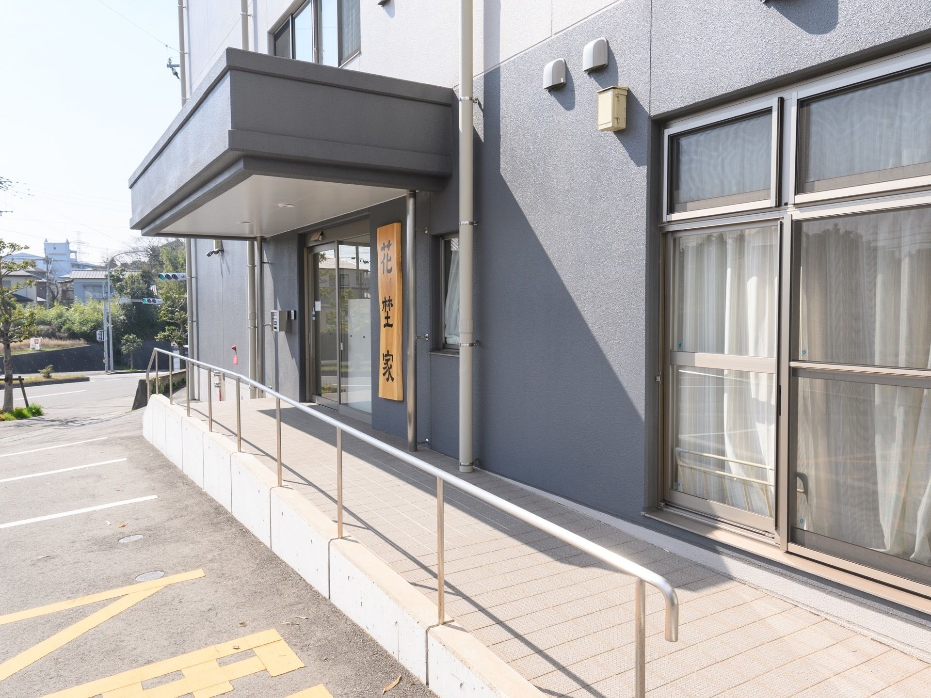 玄関ドアまでは手すりが取り付けられたスロープが設けられている。ドアの上には大きなひさしが設置されている。