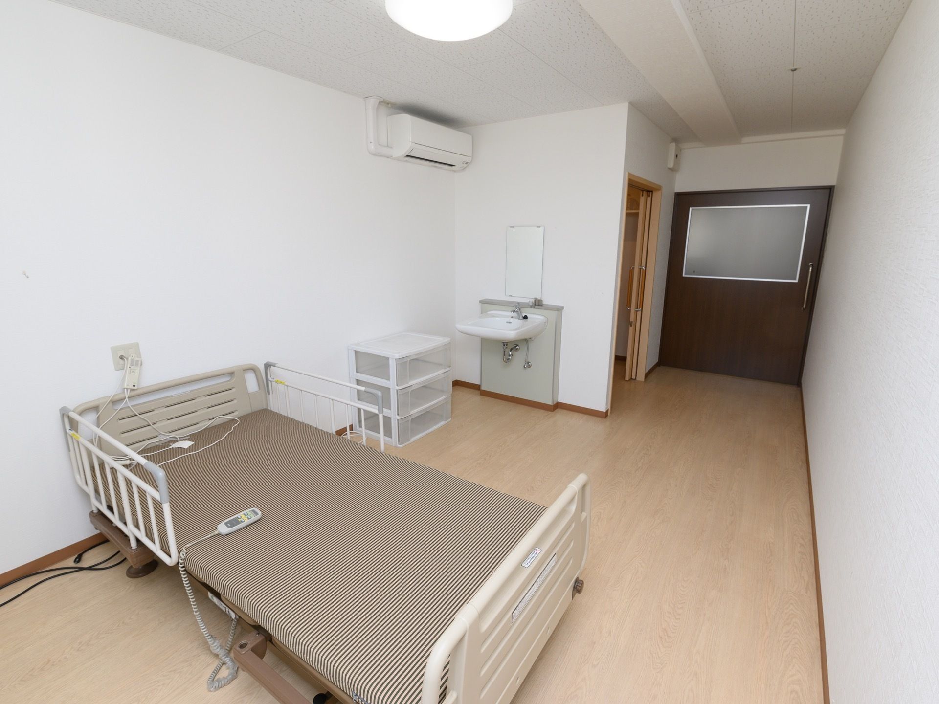 ベッド柵が取り付けられた電動ベッドが１台設置されている。鏡のついた洗面台があり、フットレス構造になっている。
