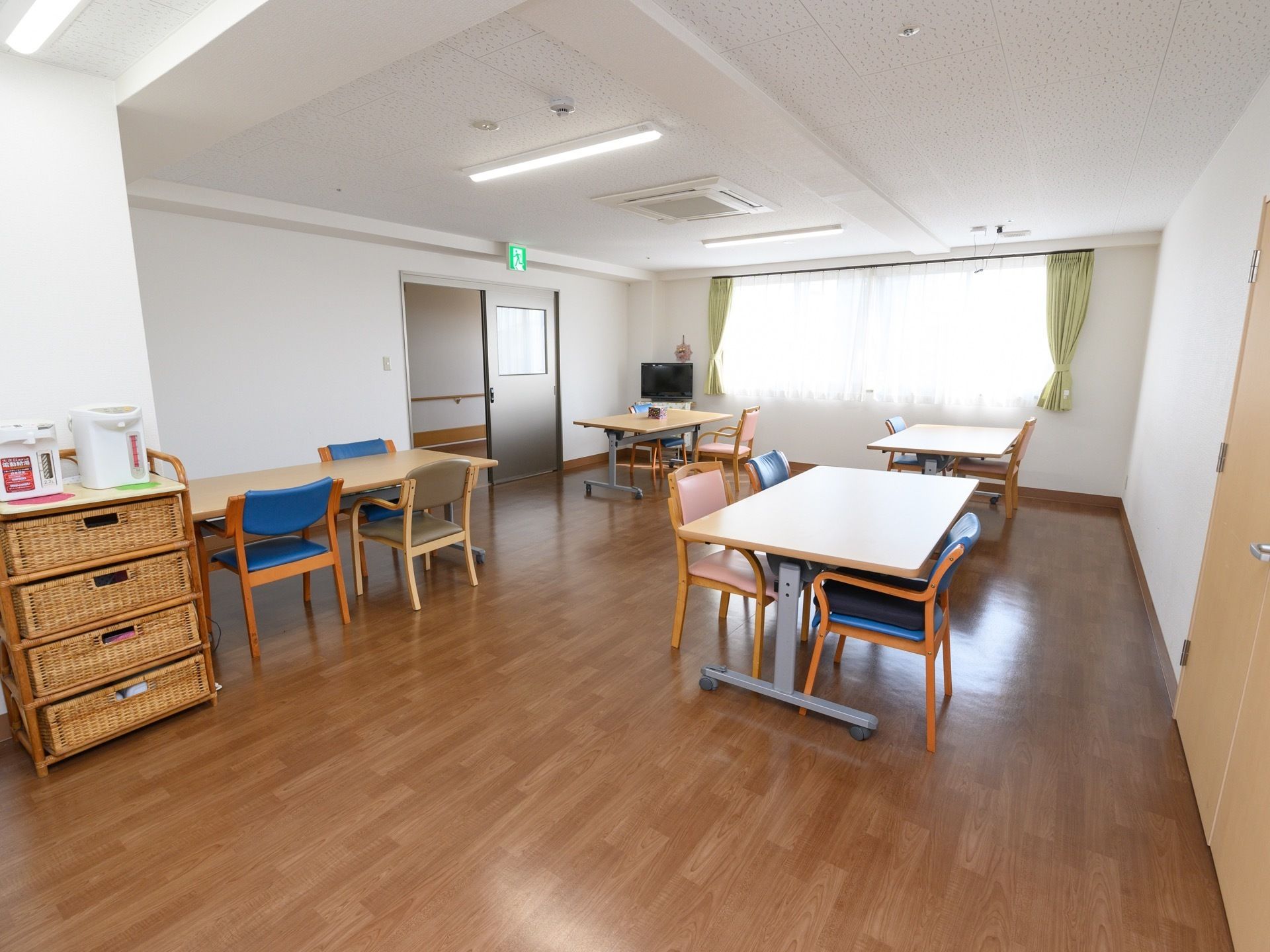 椅子とテーブルが４組並べられた、明るい食堂である。テレビが置かれ、リビングとしての役目も兼ねている。