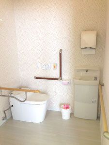 エル字型の手すりや呼び出しボタンが付いたトイレには明るい色の壁紙が貼られ、手洗い場にはペーパータオルが設置されている。