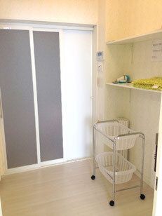 大きなドアが付いた浴室が正面にあり、コロ付きのかごラックや棚が設置されている。棚には何か黄色いものと緑のものが置かれている。