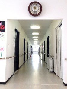 手すりが両サイドに付いたまっすぐな廊下には居室のドアも並んでいる。右側にはパネルヒーターが設置され、突き当りには大きな窓がある。