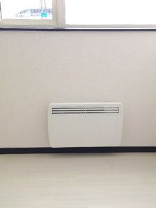白いパネルヒーターが窓の下についている。窓にはカーテンはなく、周りには家具や家電も置かれていない。窓の外は白い景色が見える。