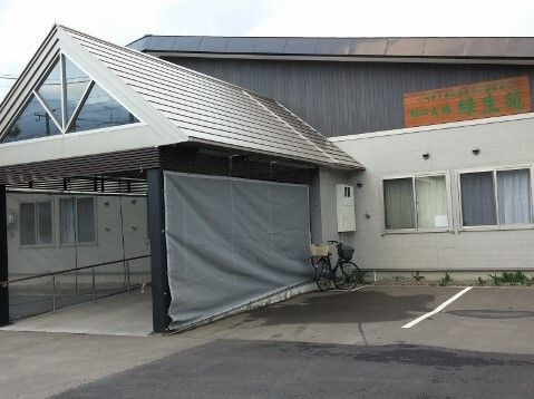 グレー系の建物の玄関には大きな車寄せが付き、周りに段差はない。敷地内には駐車スペースもある。