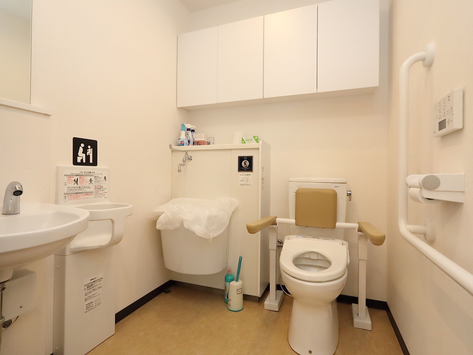 広々としたトイレには、洗面台にベビーチェア、汚物を流す専用洗面台、収納棚、L字型の手すりが設けられている。