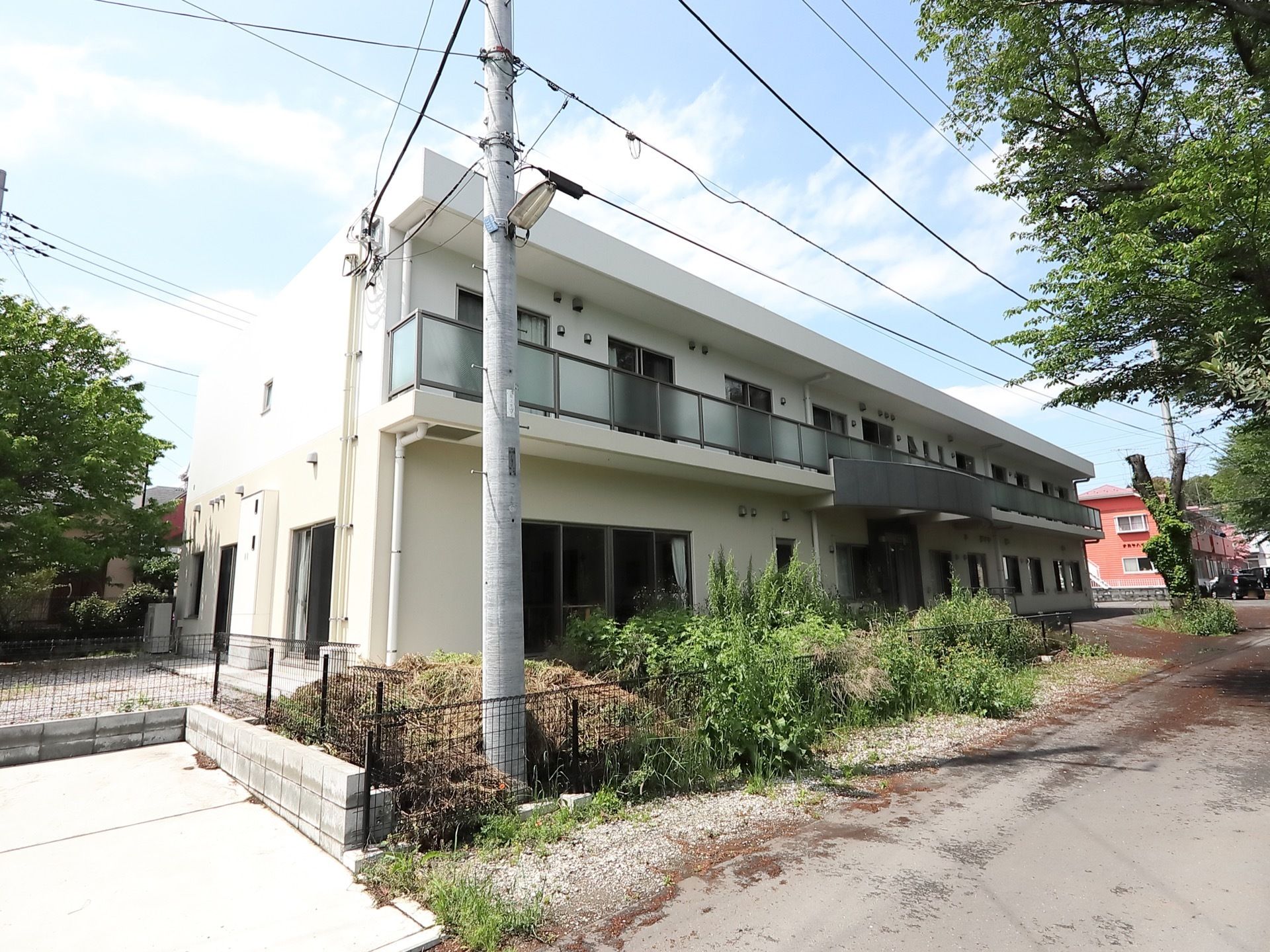 自然の多い、閑静な住宅街に建つ施設の外観である。２階の各部屋には、広いベランダが設置されている。道路から玄関先まで段差がない。