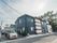 青い外壁の２階建ての施設。左側の舗装されたスペースには複数の自動車が駐車されており、建物の左側には高木がある。