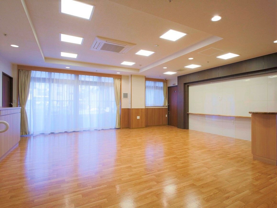 広々としたフローリングの共有スペース。家具などはなく、大きな窓にはカーテンとレースカーテンが設置されている。