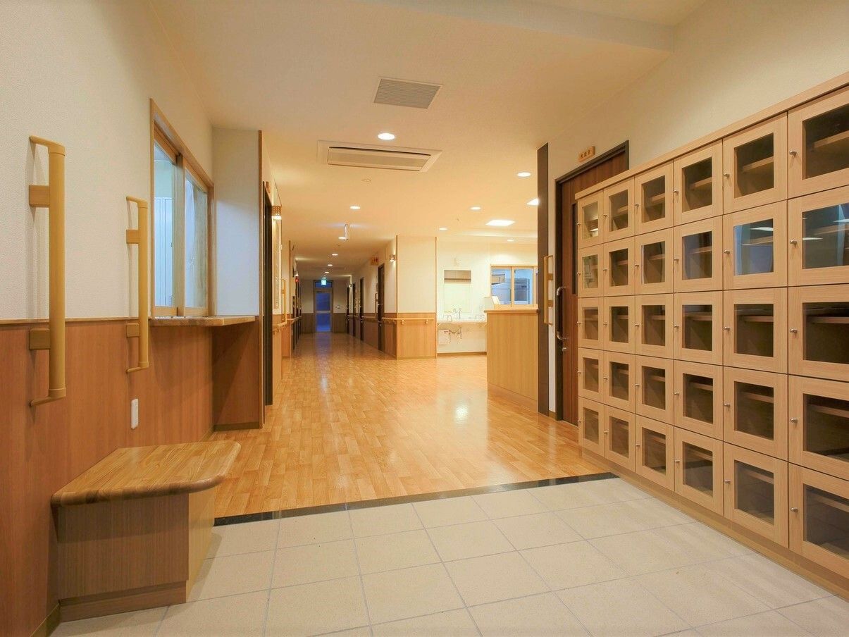 扉付きの大きな靴箱が右側にあり、左側に手すり付きのベンチが置かれ、段差を解消している玄関。正面には廊下が続いている。