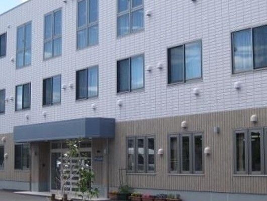 3階建ての建物。グレー系の色でまとめられていて、玄関には屋根が付き、植物も植えらえている。