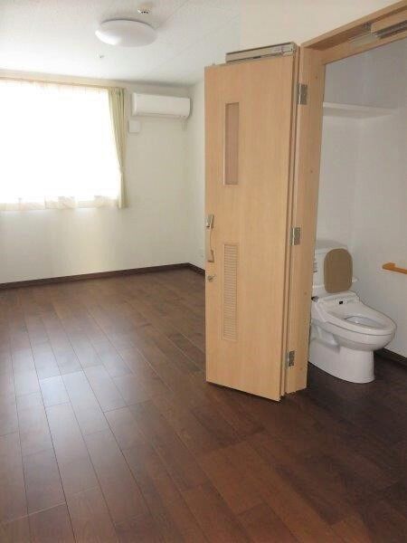 手前にトイレが置いてある施設内の居室の様子。バリアフリーの床と奥の方にエアコンがある